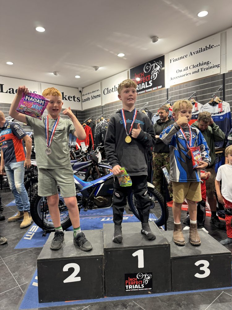 Three boys with medals on podiums holding candy bags in a motorcycle store.