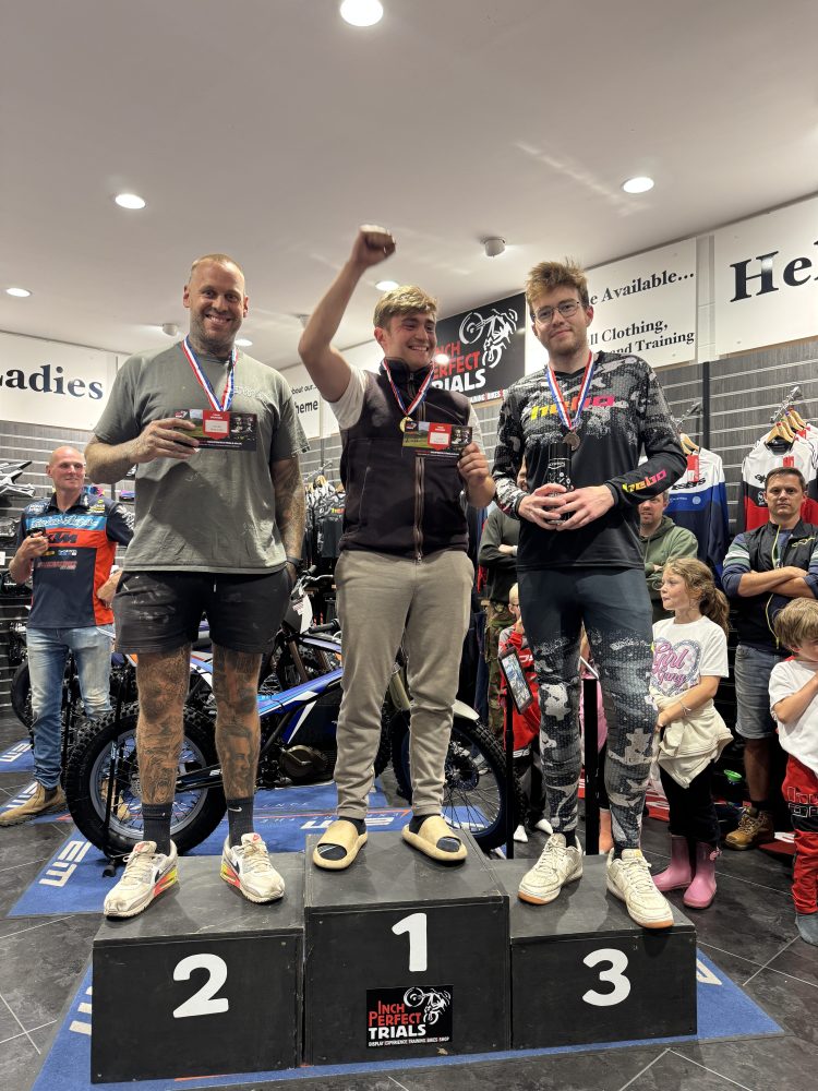 Three men on a winners' podium inside a store, wearing medals and holding certificates.