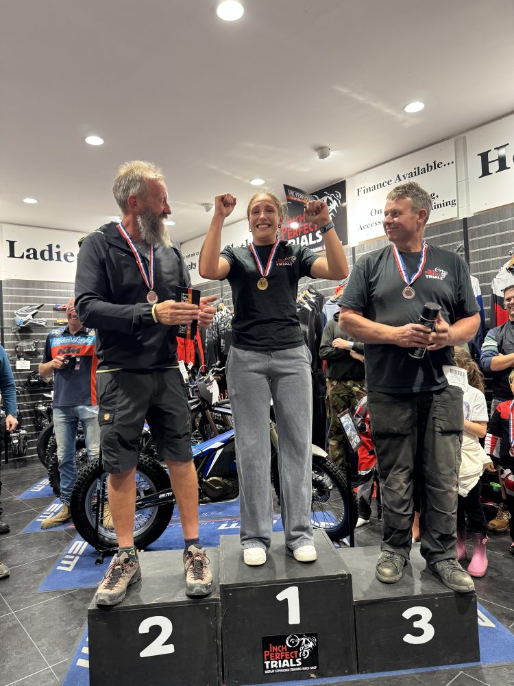 Three people on a winners podium celebrating with medals in a motorcycle store.