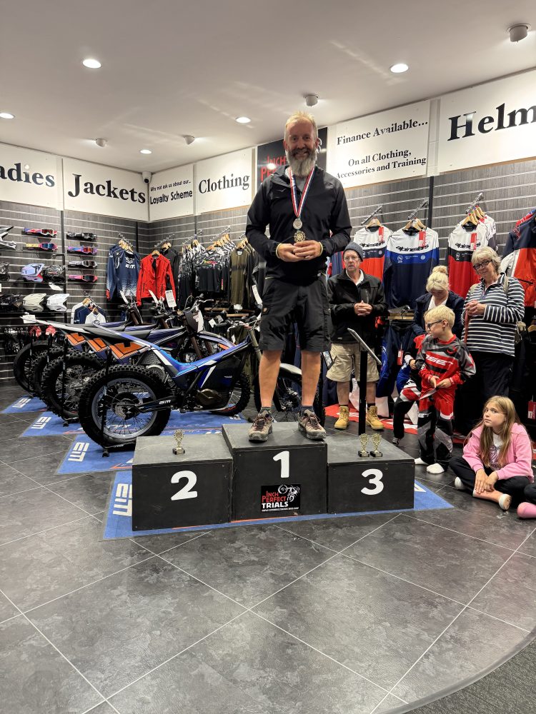 Man on podium with medal, surrounded by people and motorbikes in a store.