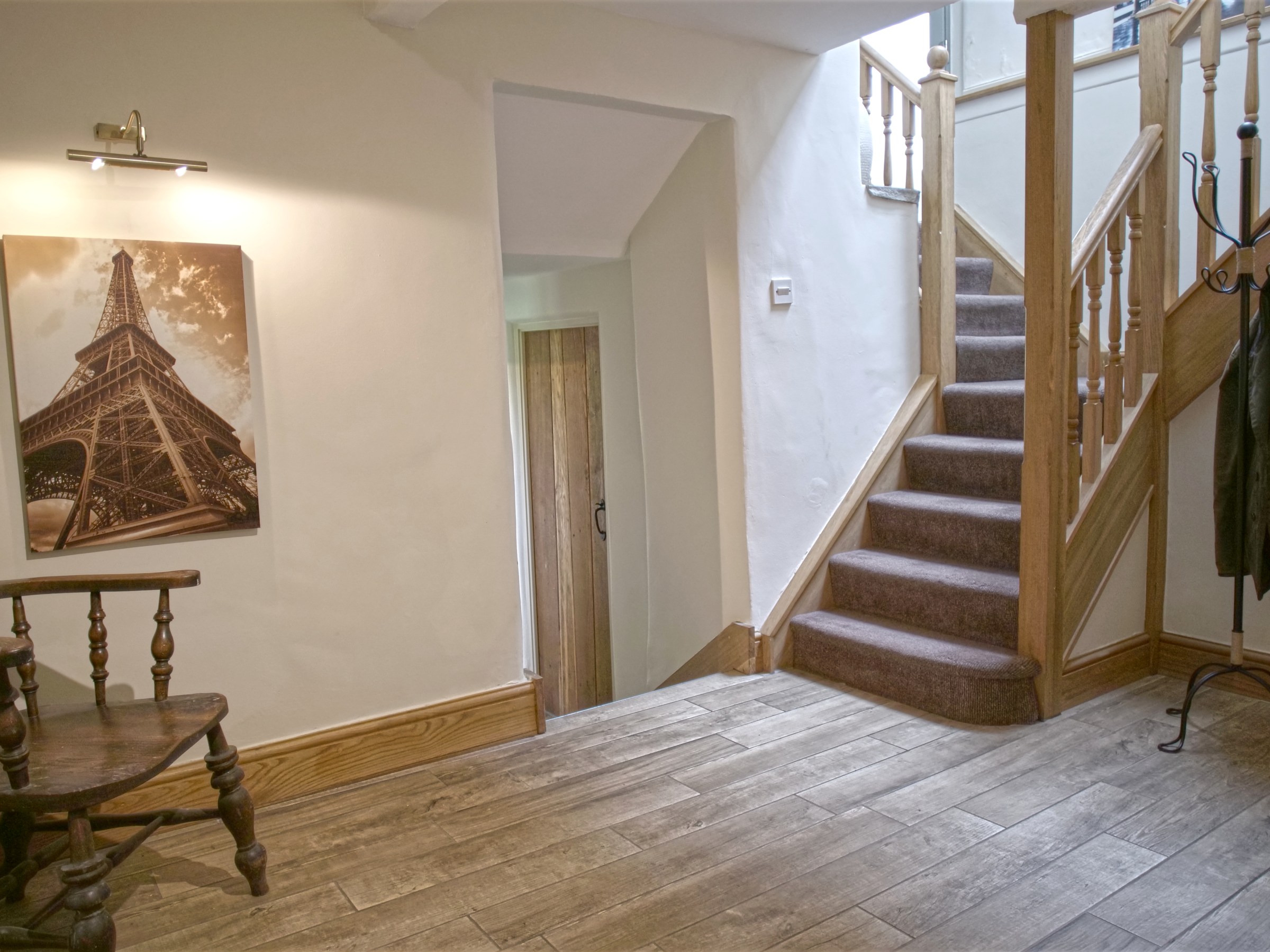 Hallway with wooden chair, Eiffel Tower photo, staircase, and coat rack.