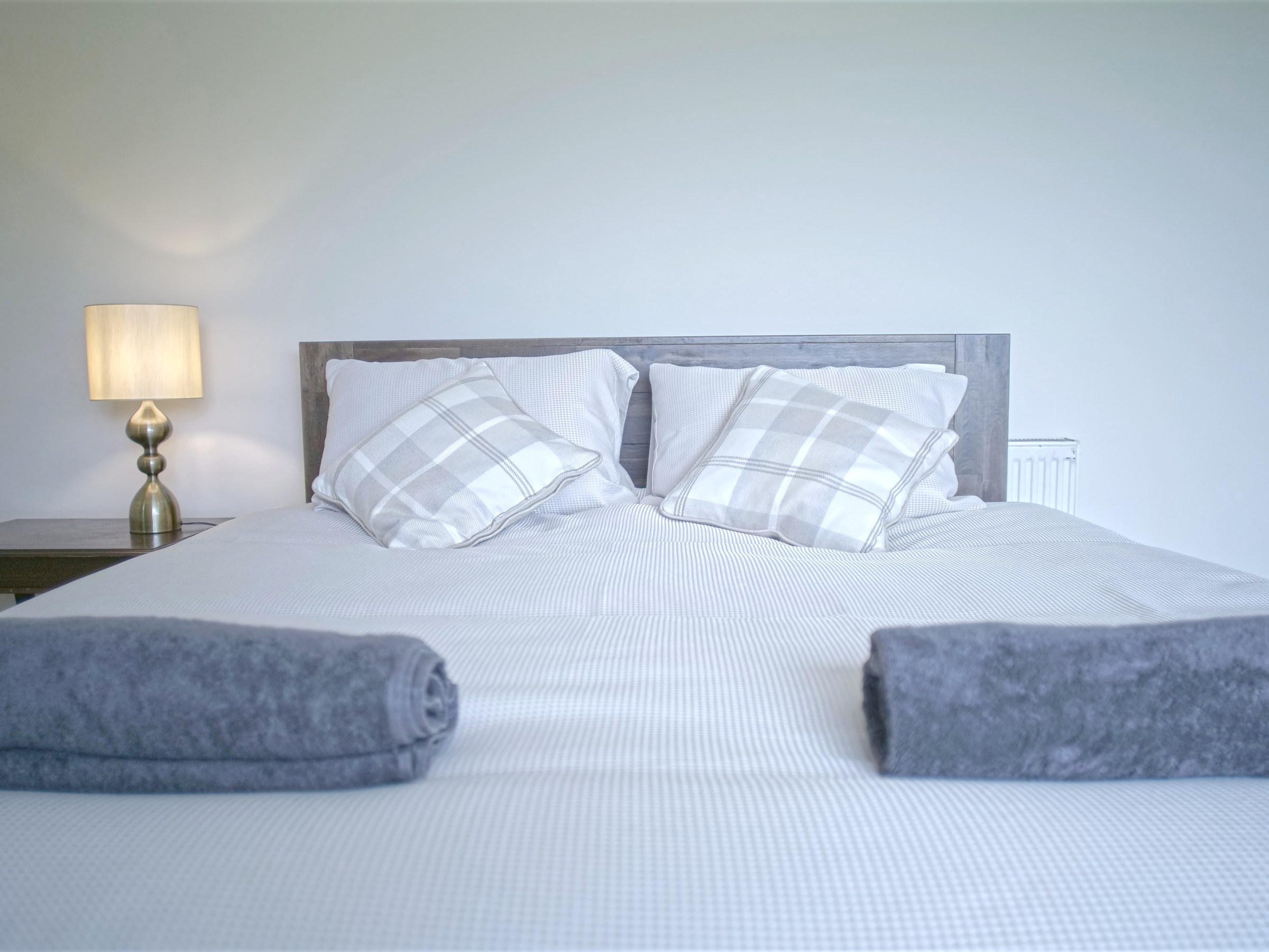 Minimalist bedroom with a double bed, two plaid pillows, and a lamp on a side table.