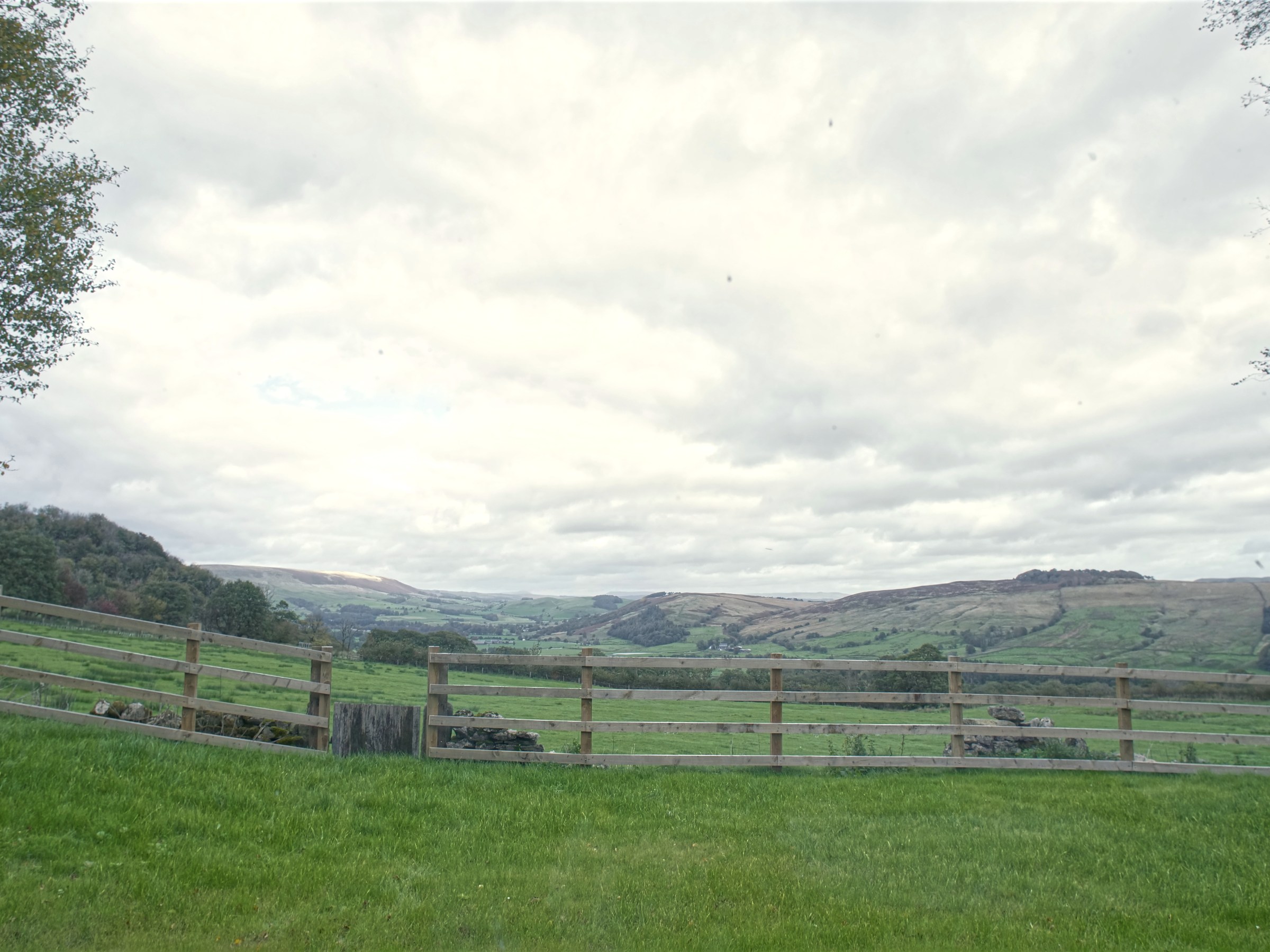 Scenic view of rolling hills and fields with a wooden fence under cloudy skies.