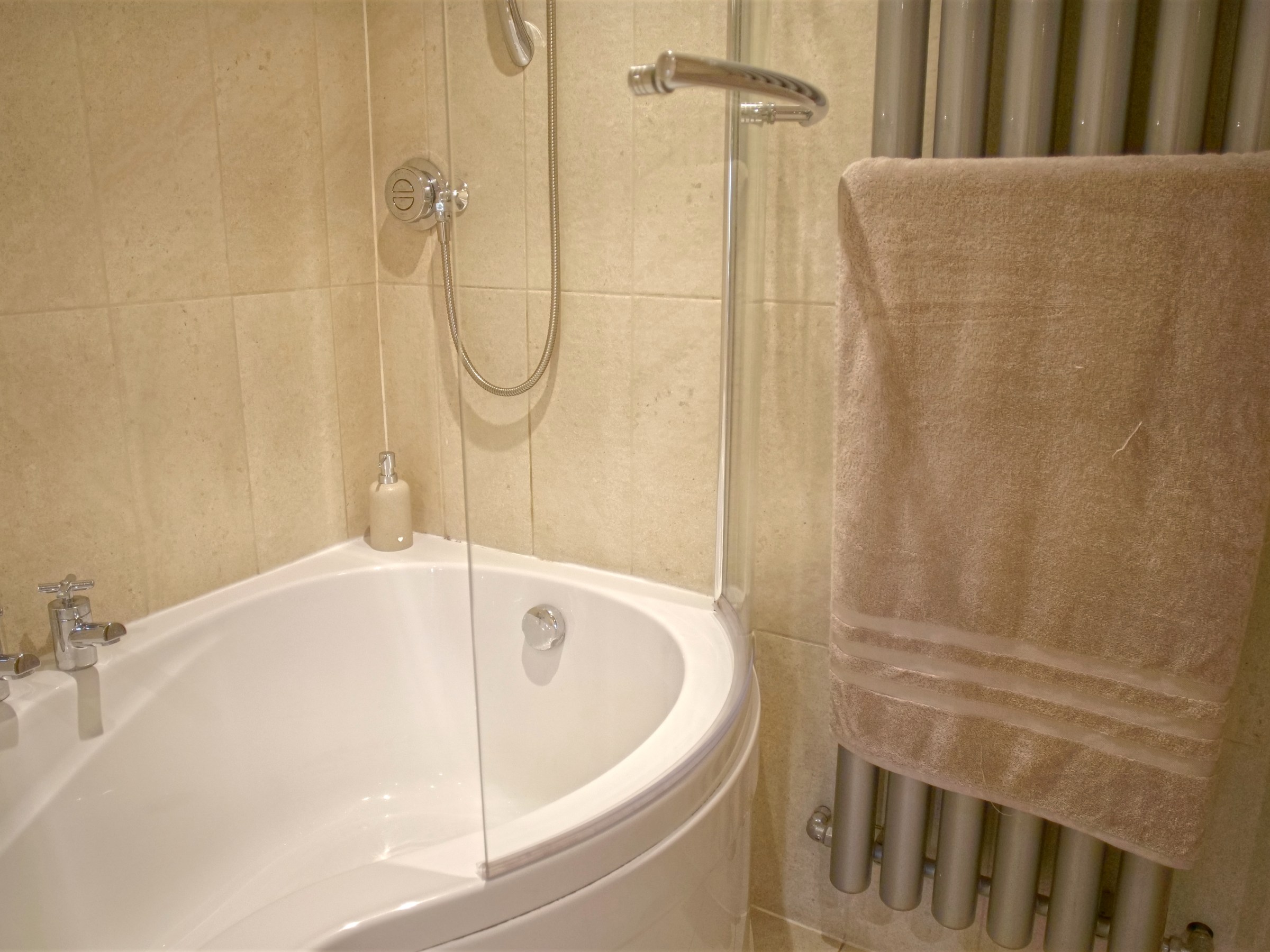 Corner bathtub with showerhead, glass screen, and towel on radiator.