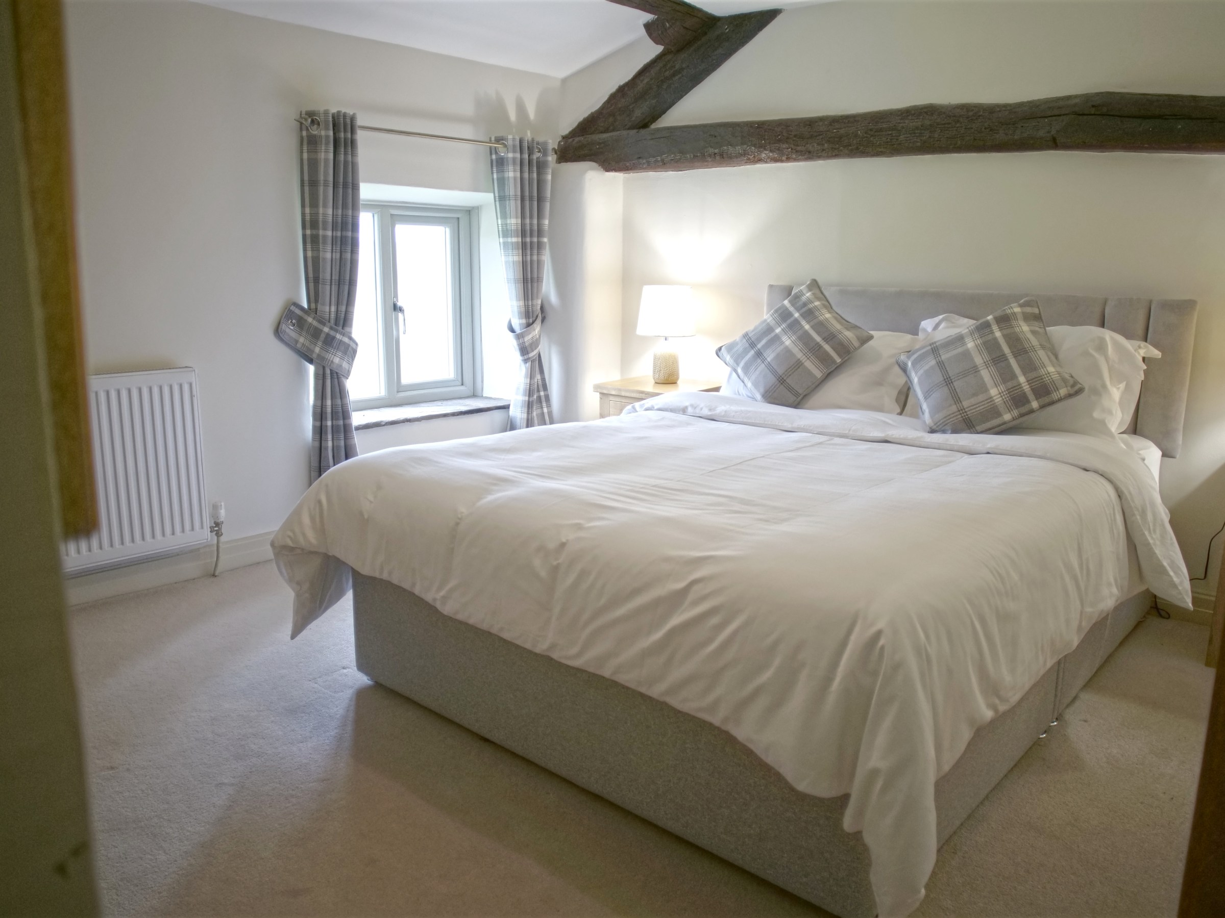 Cozy bedroom with exposed beam, double bed, plaid pillows, and window with curtains.