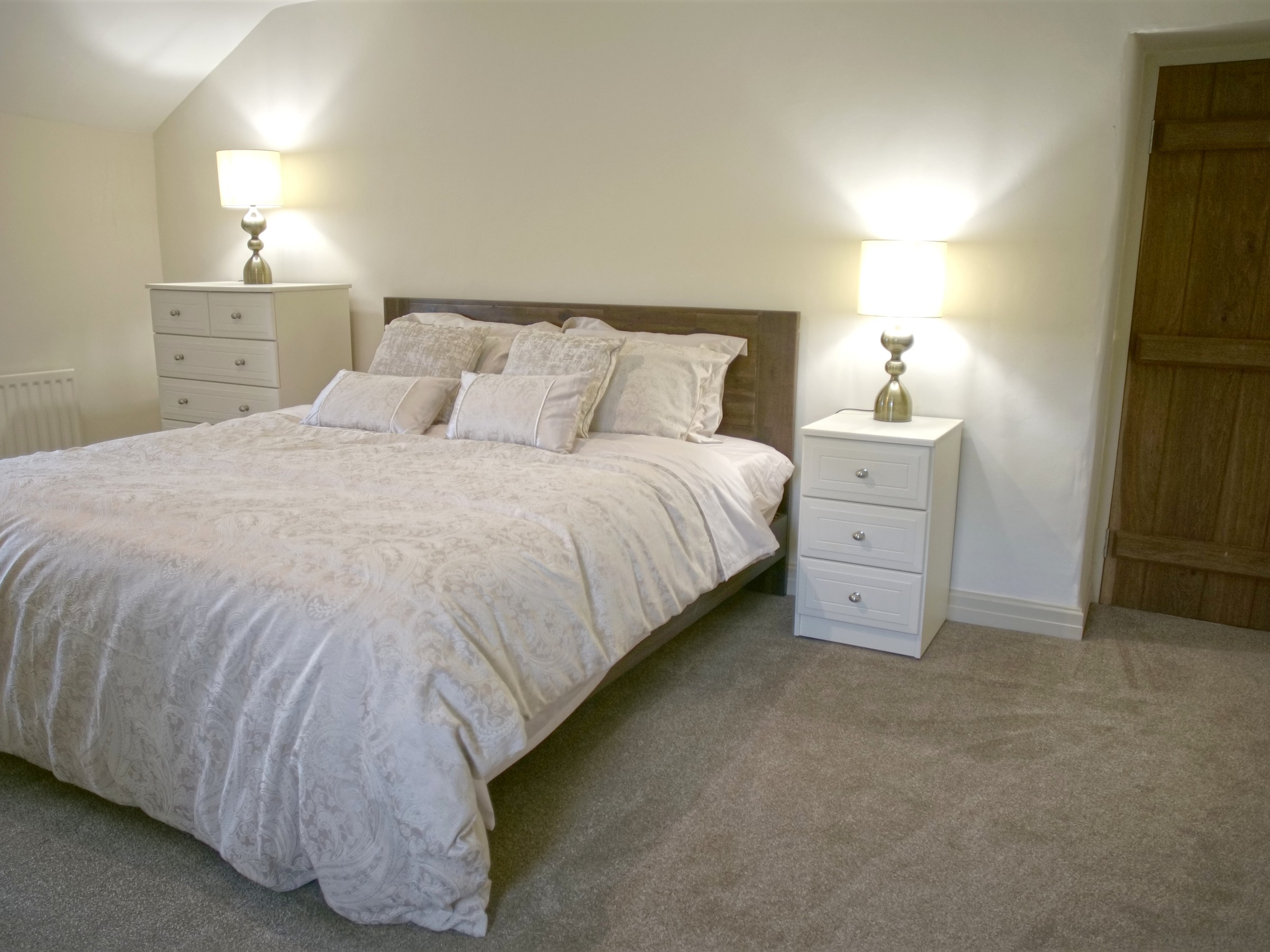 Cozy bedroom with a bed, two dressers, and soft lighting.