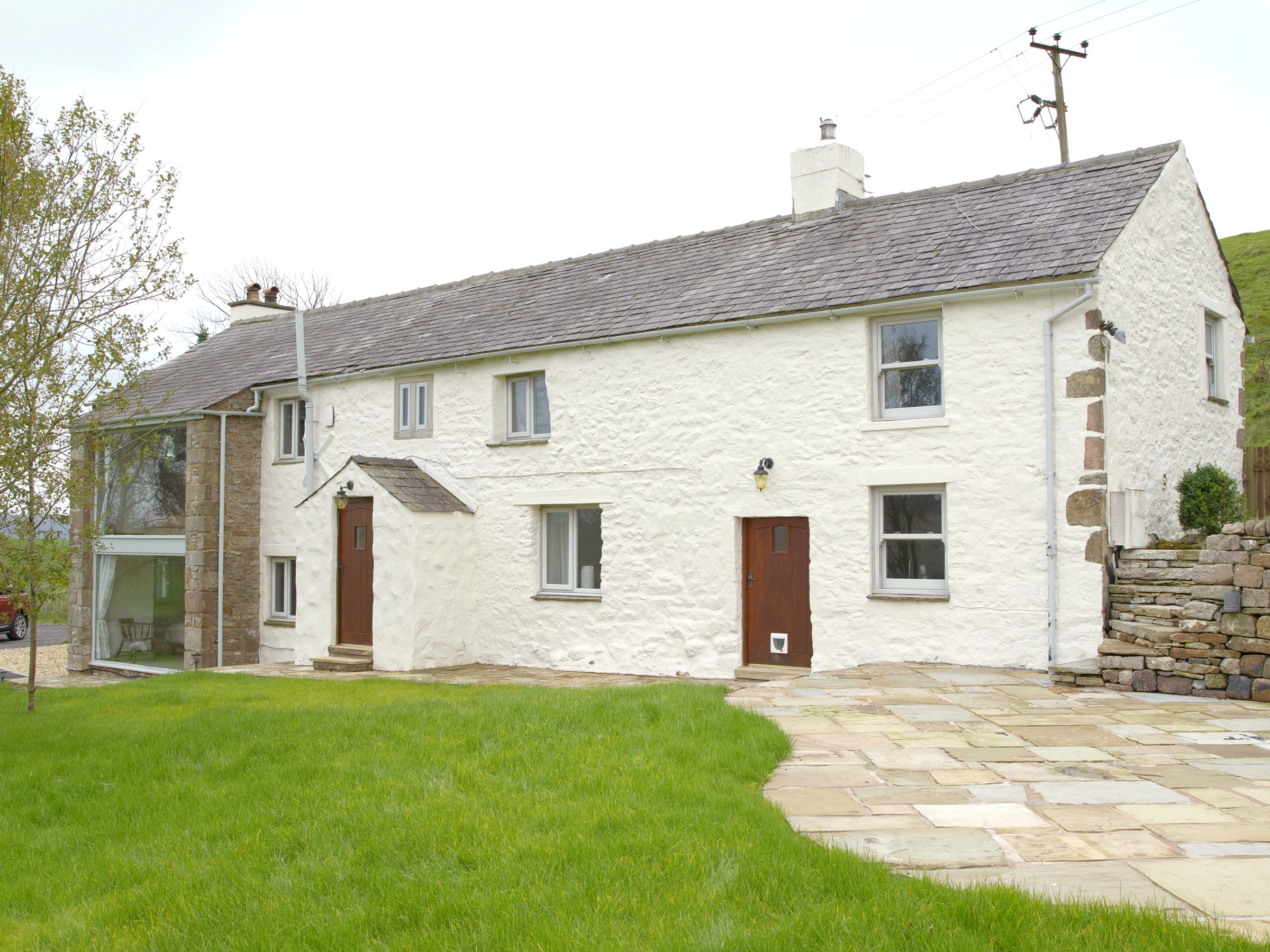 White stone cottage with two floors, wooden doors, large windows, and a green lawn.